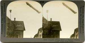 Horizontale, sepiafarbene Stereokarte, die ein Zeppelin zeigt, der über die Dächer einer Stadt fliegt. Keystone Stereograph Nummer 18000. Der Titel lautet von Keystone View Company